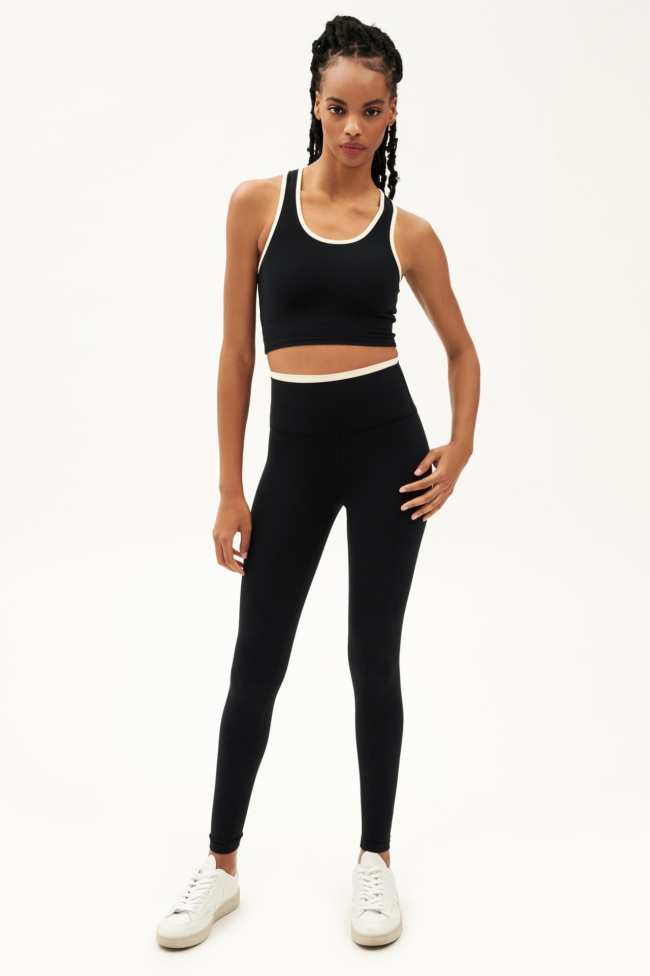Full front view of girl wearing black leggings with thin white band around waist and black tank top with white shoes