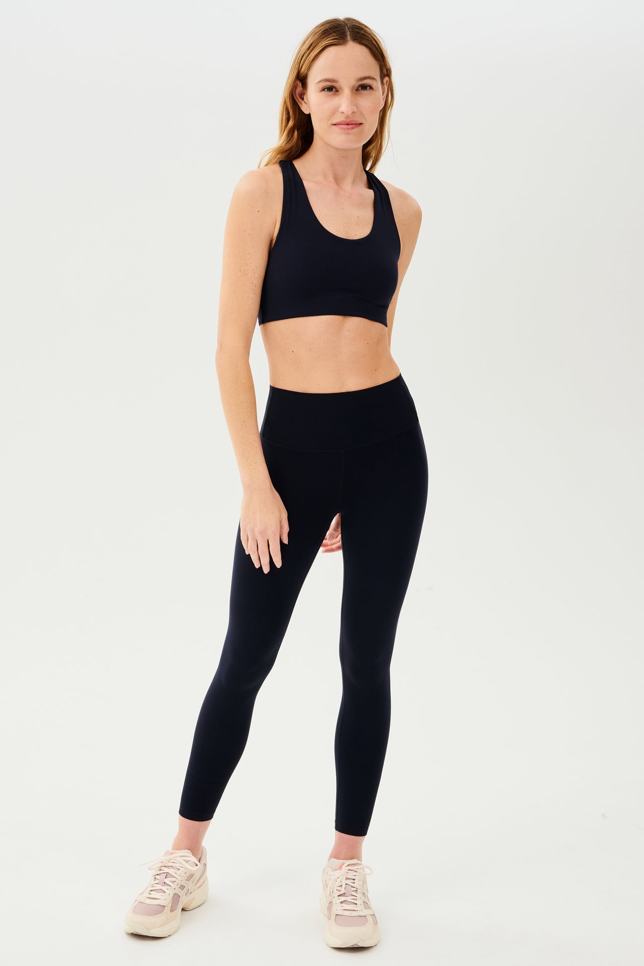 Full front view of girl wearing  highwasited dark blue leggings with dark blue sports bra pink and cream shoes