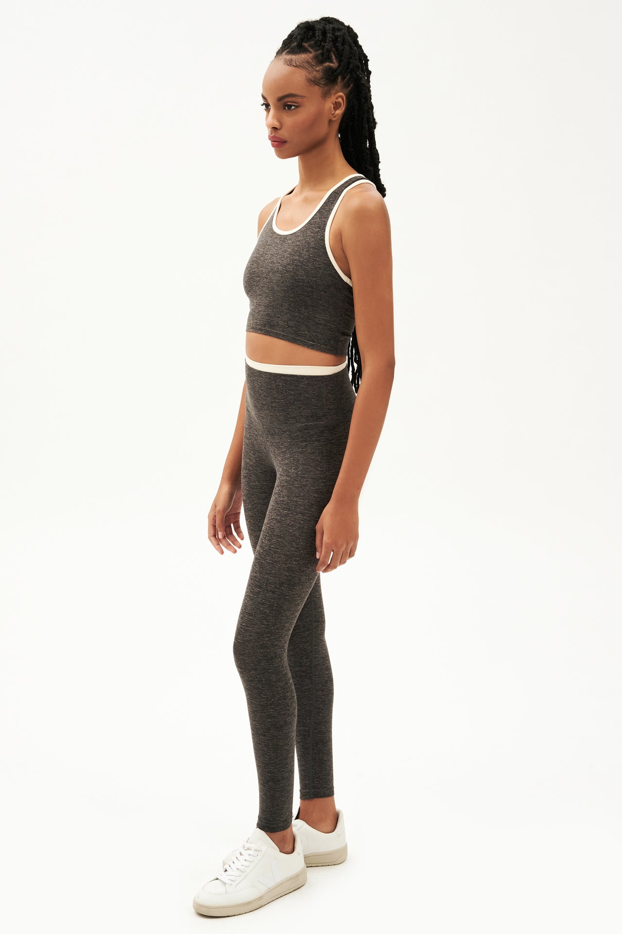 Full side view of girl wearing dark grey leggings with thin white band around waist and dark grey tank top with white shoes
