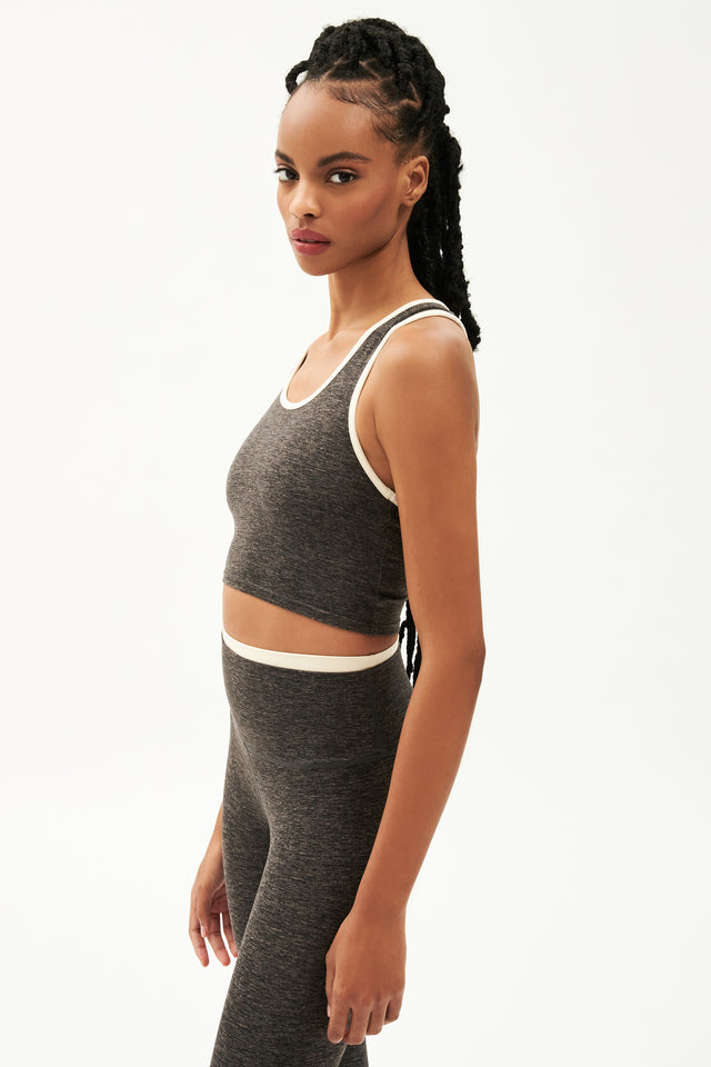 Side view of girl wearing cropped grey tank top with white trim and grey leggings with a thin white waistband