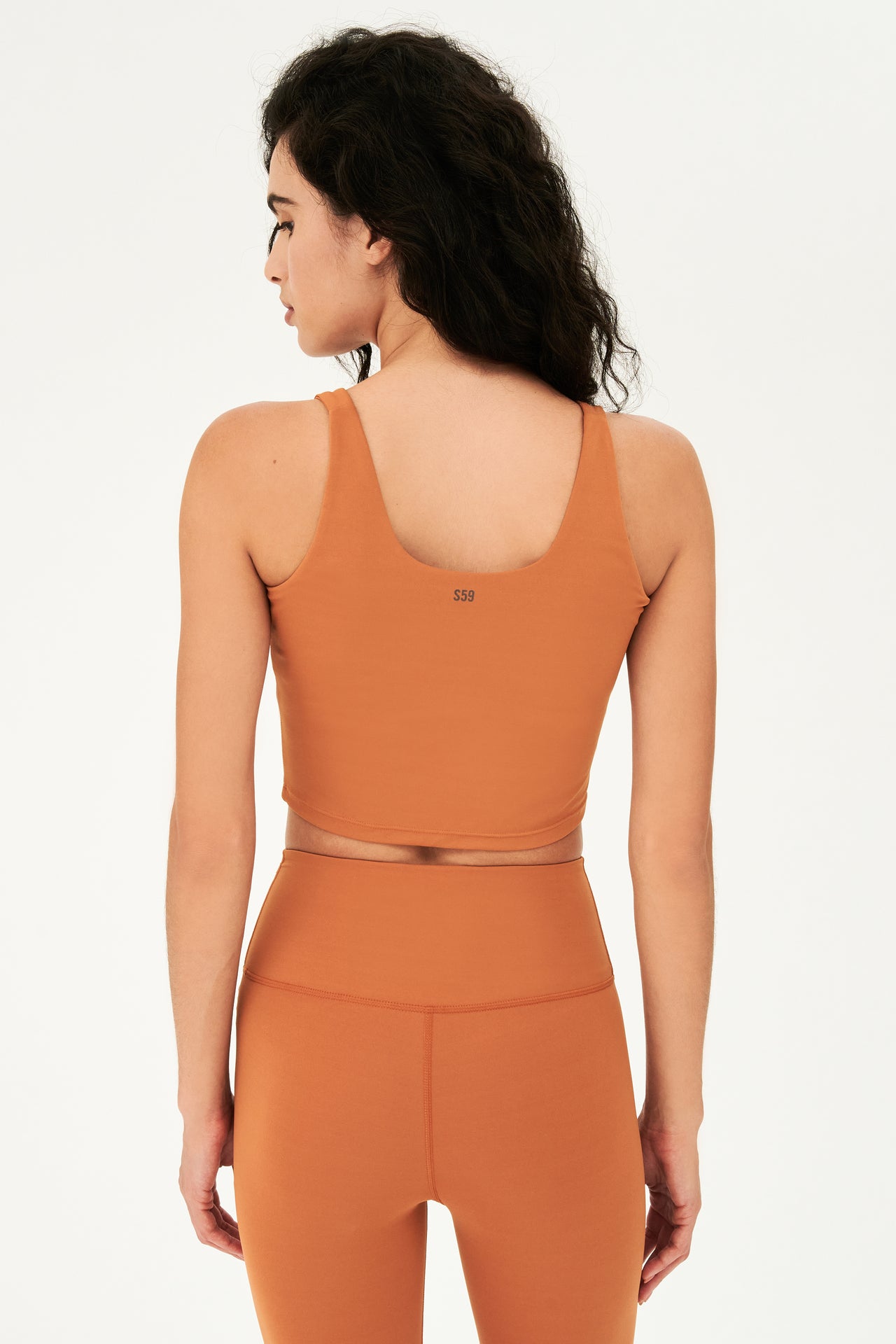 Back view of woman with curly dark brown hair wearing a dark orange bra tank  with dark orange leggings