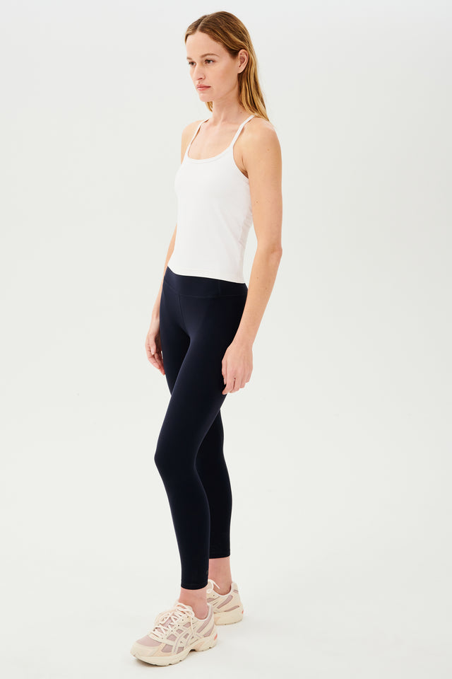Full side view of girl wearing white spaghetti strap tank top with black leggings and white shoes