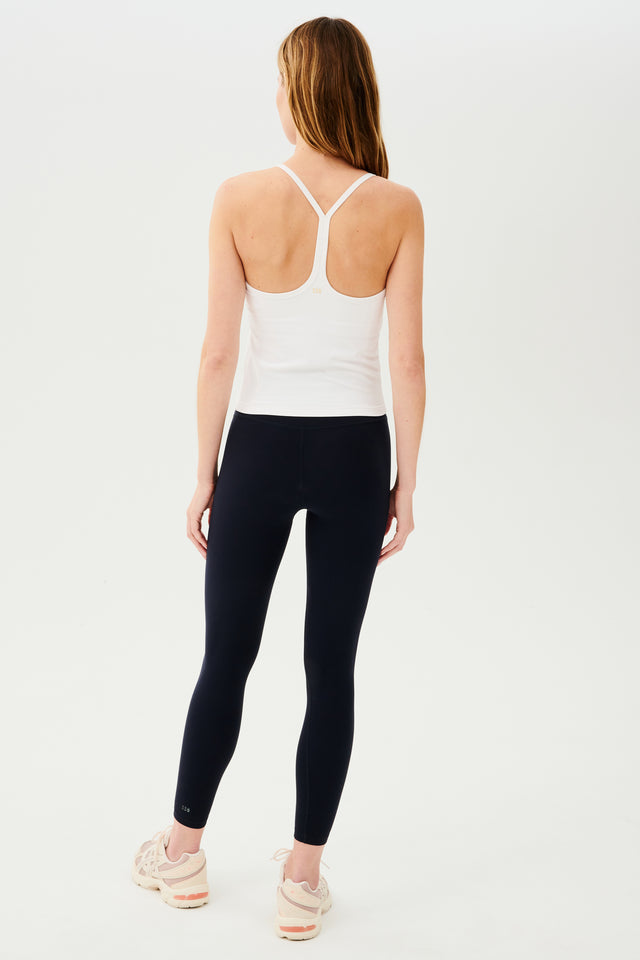 Full back view of girl wearing white spaghetti strap tank top with black leggings and white shoes
