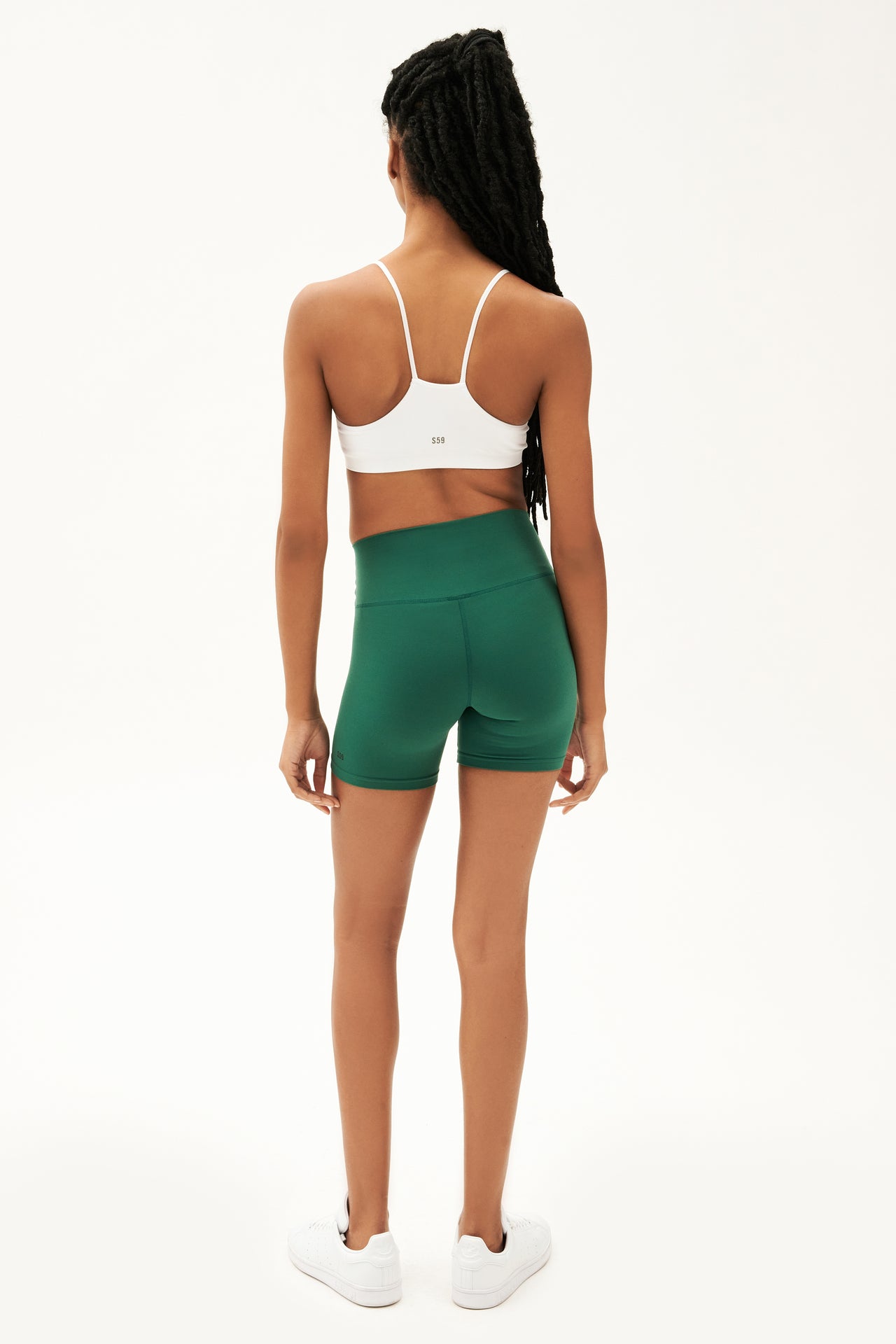 Full back view of girl wearing highwaisted mid thigh green bike shorts with white sports bra and white shoes