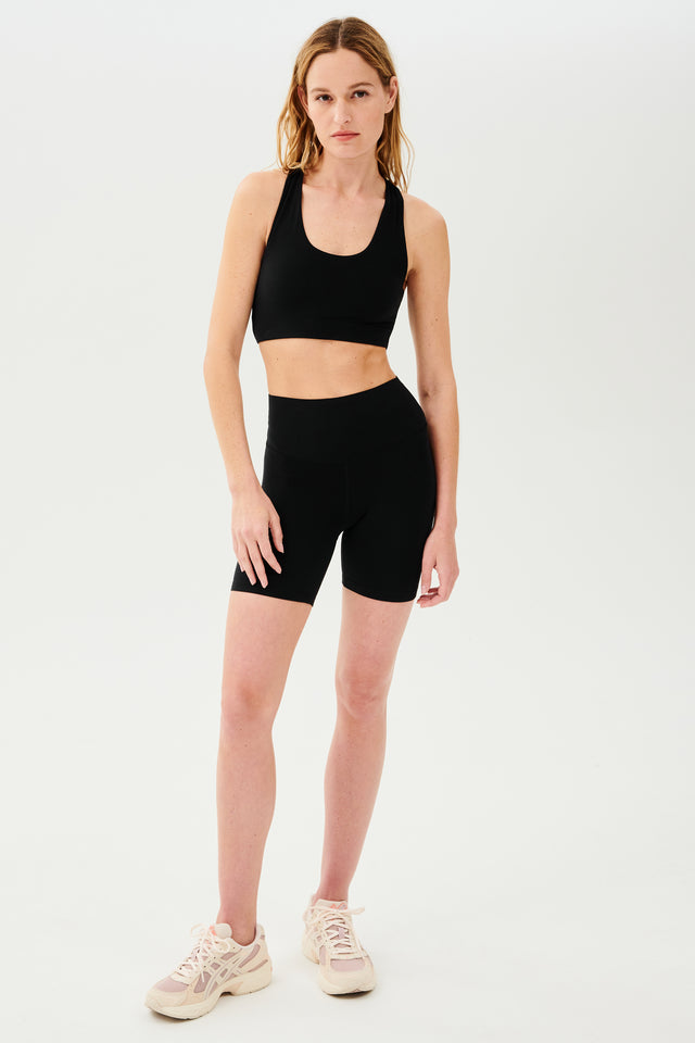 Full front view of girl wearing highwaisted mid thigh black bike shorts with black sports bra and  white shoes