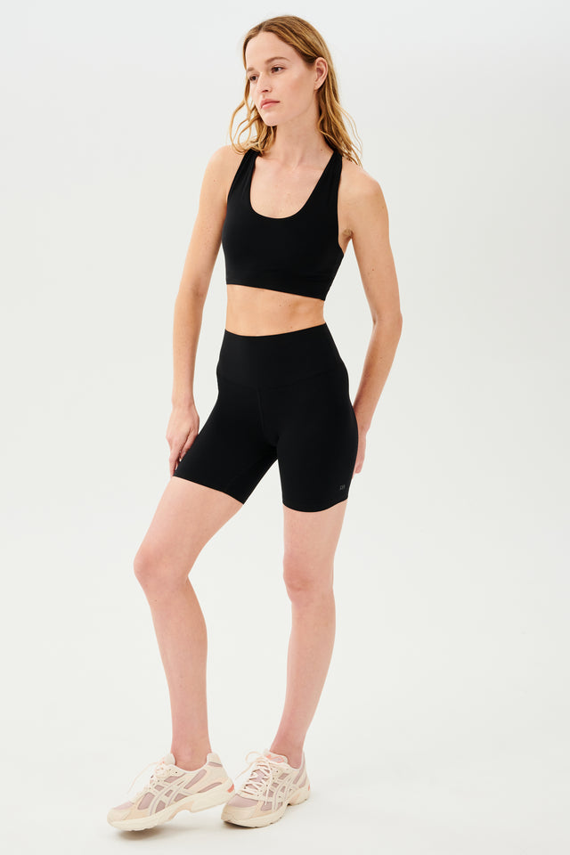 Full side view of girl wearing highwaisted mid thigh black bike shorts with black sports bra and white shoes