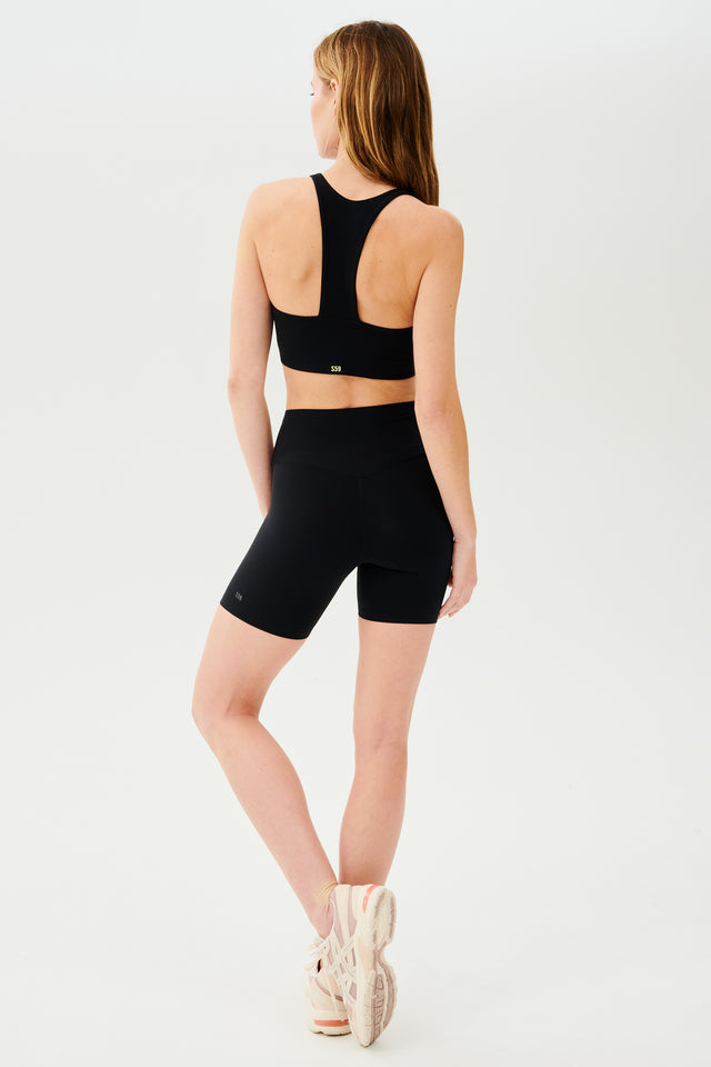 Full back view of girl wearing highwaisted mid thigh black bike shorts with black sports bra and white shoes
