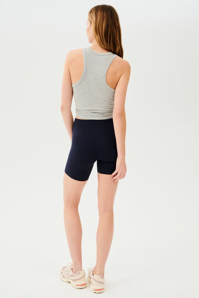 Full back view of girl wearing highwaisted mid thigh dark blue bike shorts with light grey tank top and white shoes