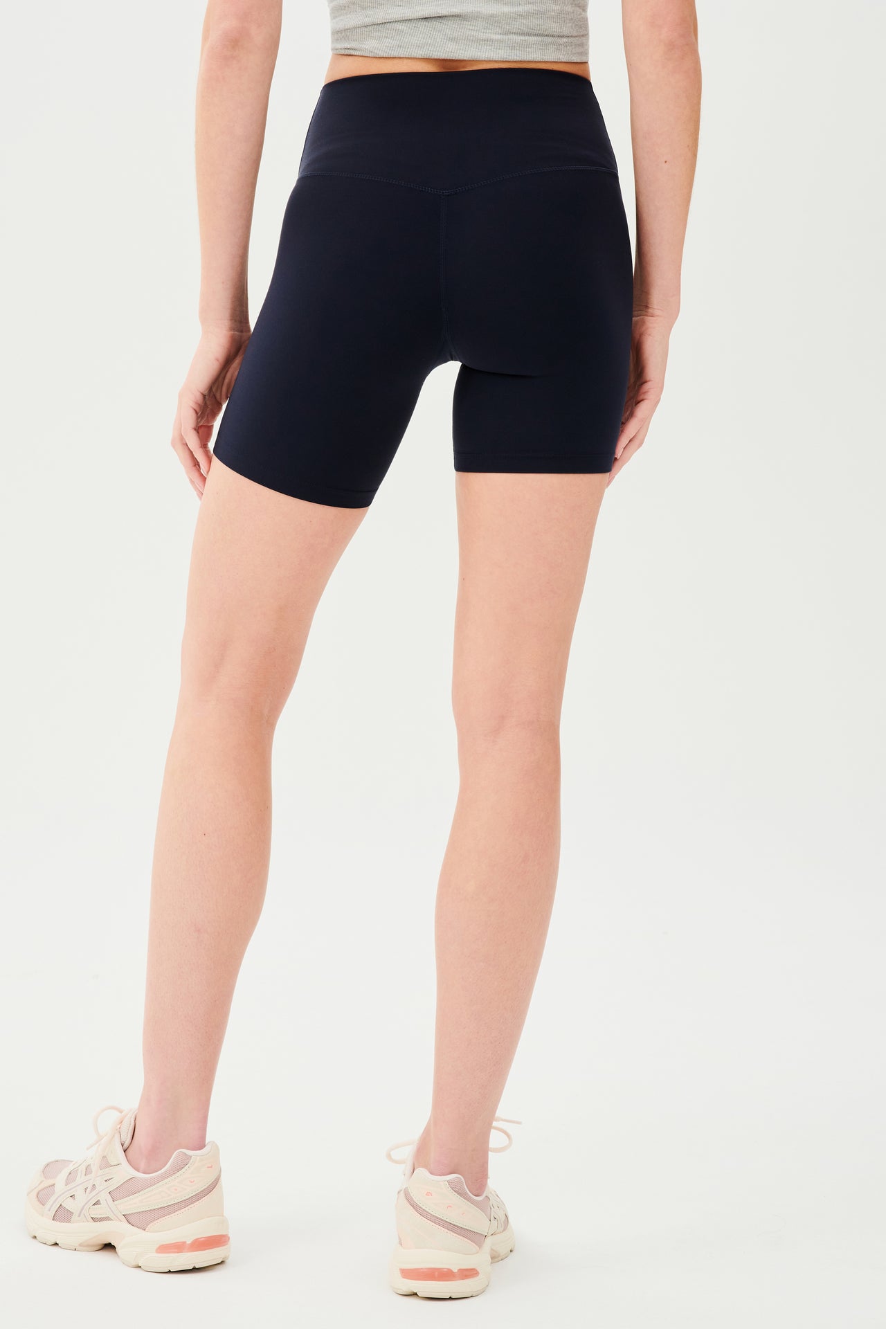 Back view of girl wearing highwaisted mid thigh dark blue bike shorts with white shoes