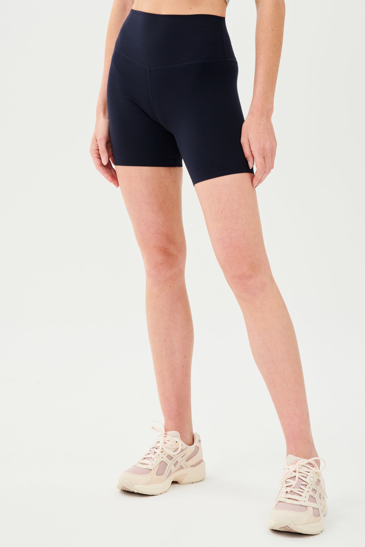 Side view of girl wearing highwaisted mid thigh dark blue bike shorts with white shoes