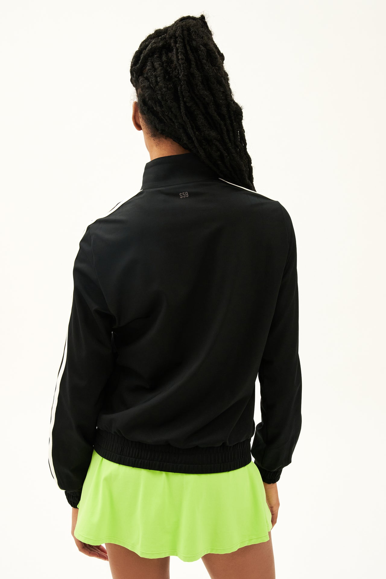 Back view of girl wearing black zip jacket that stops under chin with two white stripes down the side  with a  green skirt