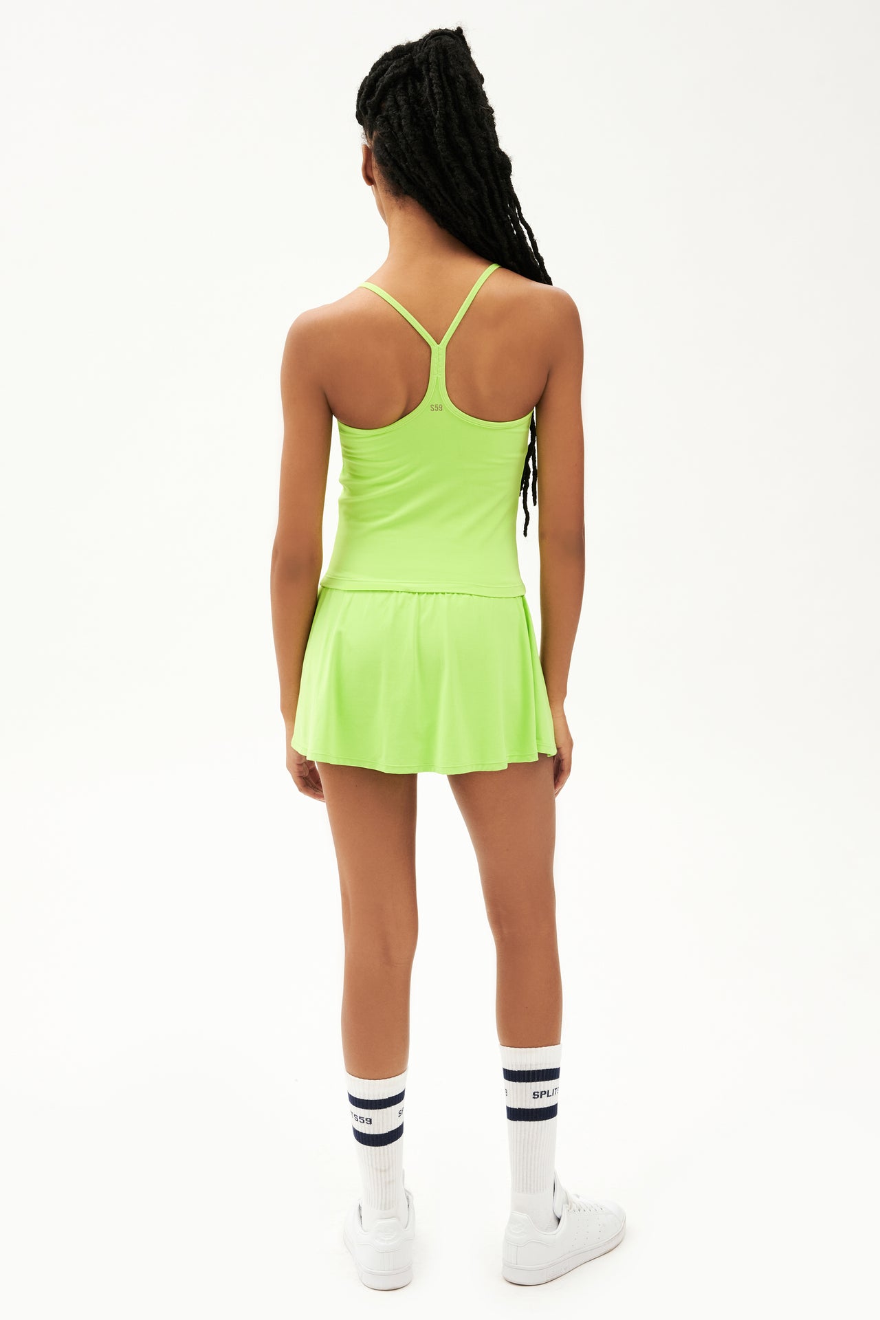 Full back view of neon green upper thigh skirt with built in shorts, neon green tank top and white shoes