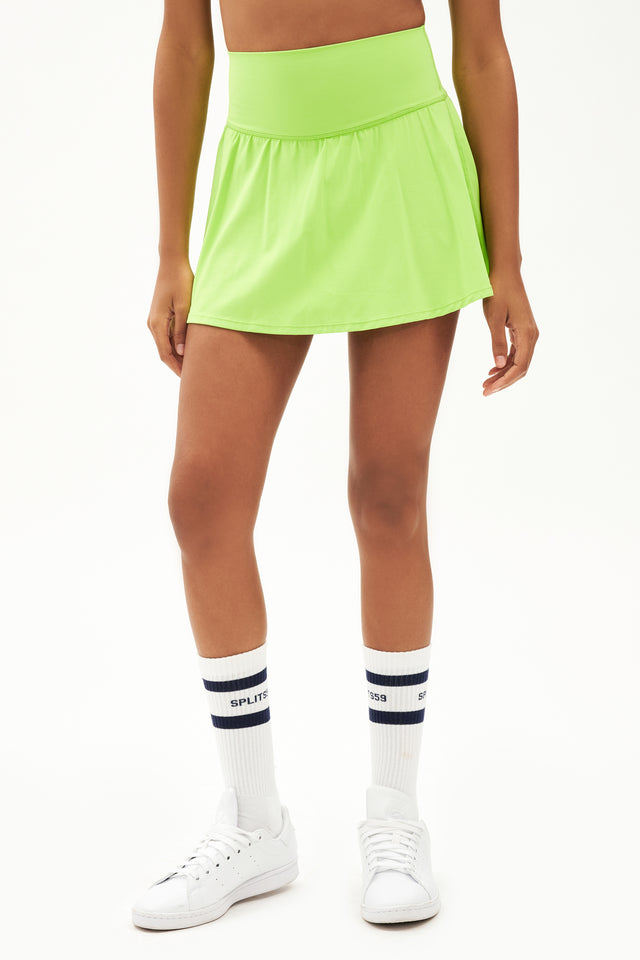 Front view of girl wearing neon green upper thigh skirt with built in shorts and white shoes