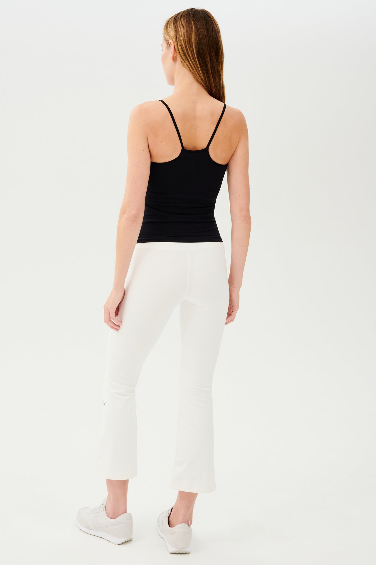 The back view of a woman wearing a black tank top and white SPLITS59 Raquel High Waist Crop.