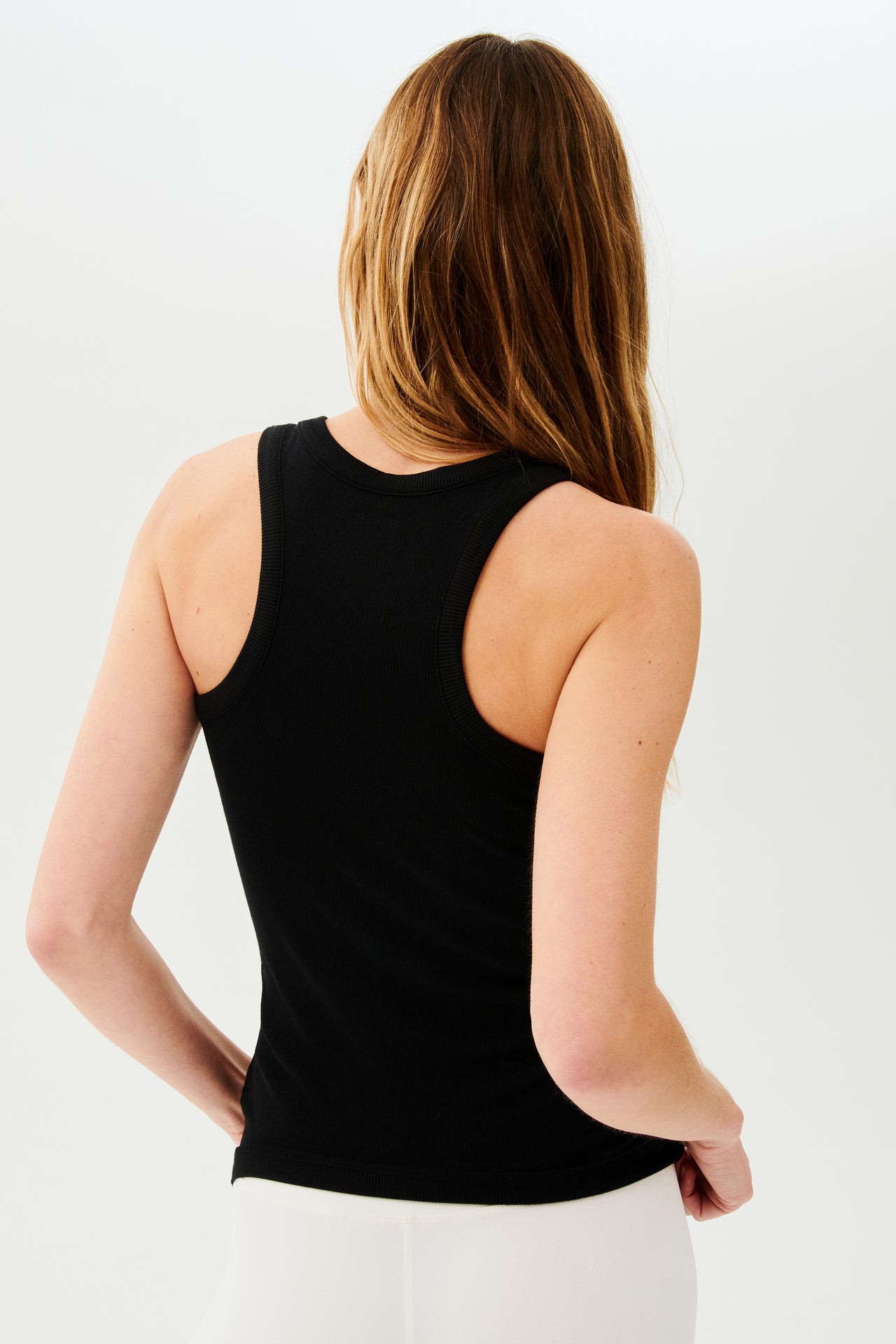 The back view of a woman wearing a SPLITS59 Kiki Rib Tank Full Length - Black during her gym workouts.