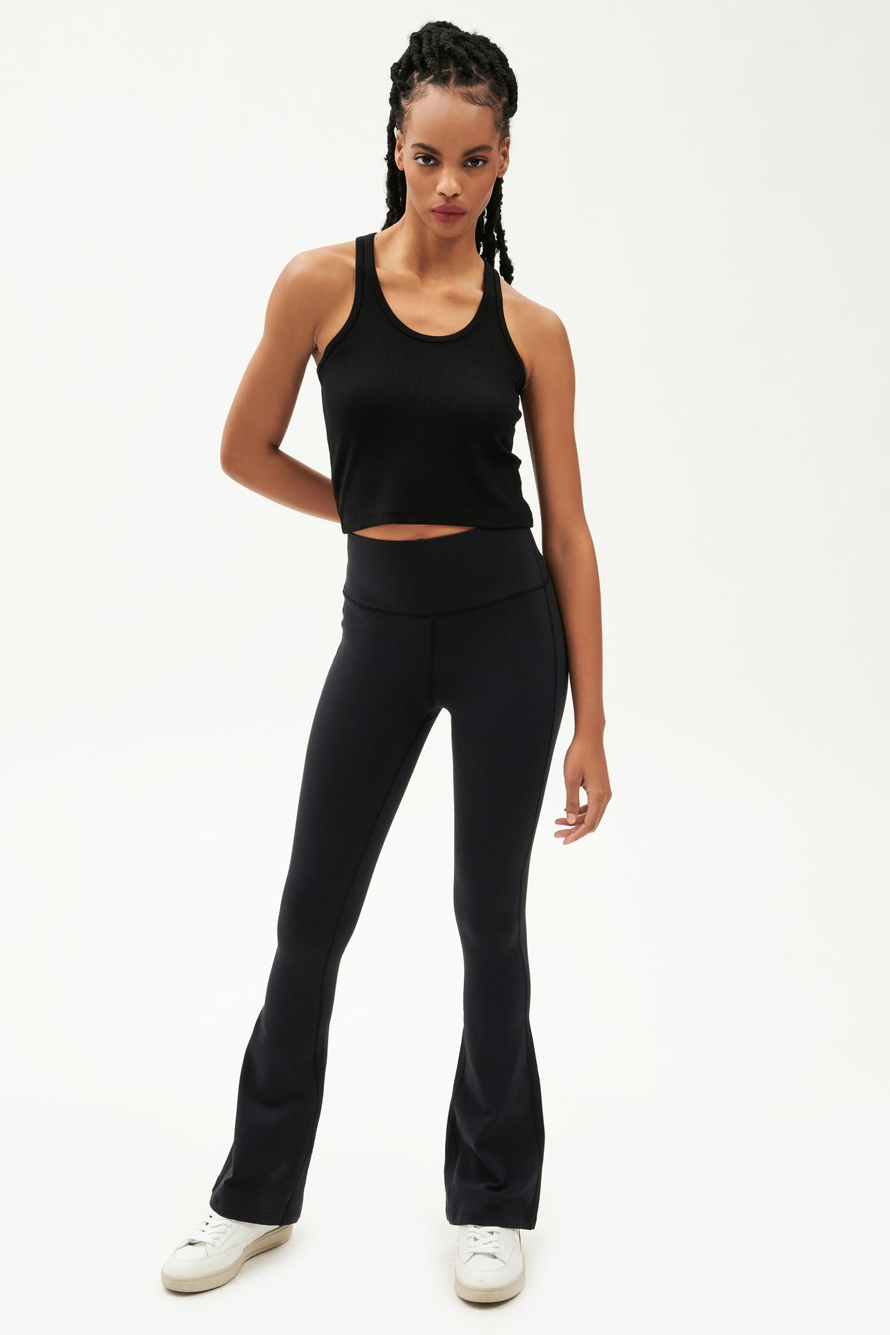 Front view of girl wearing a ribbed black cropped tank top and black flared leggings with white shoes