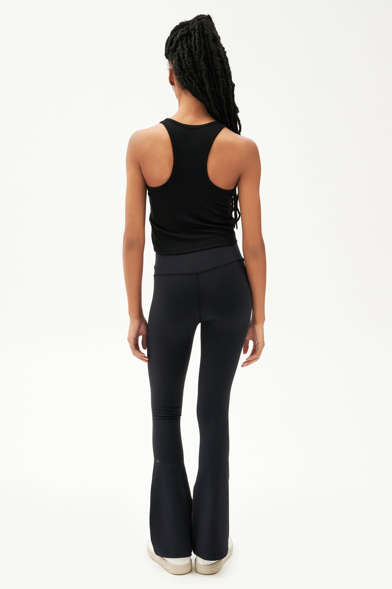 Full back view of girl wearing a ribbed black cropped tank top and black flared leggings with white shoes