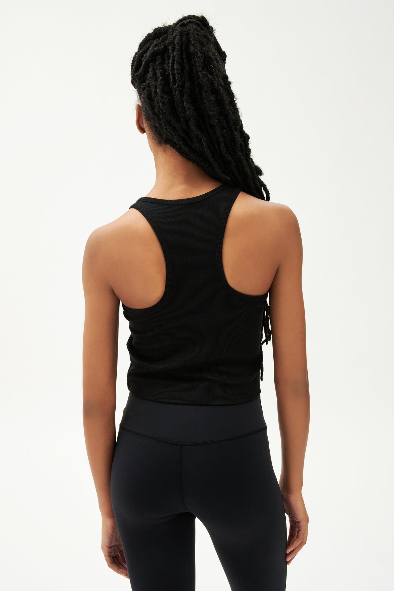 Back view of girl wearing a ribbed black cropped tank top and black leggings 