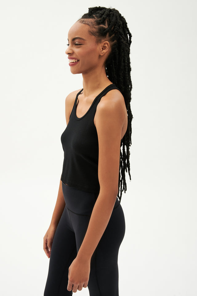 Side view of girl wearing a ribbed black cropped tank top and black leggings with white shoes