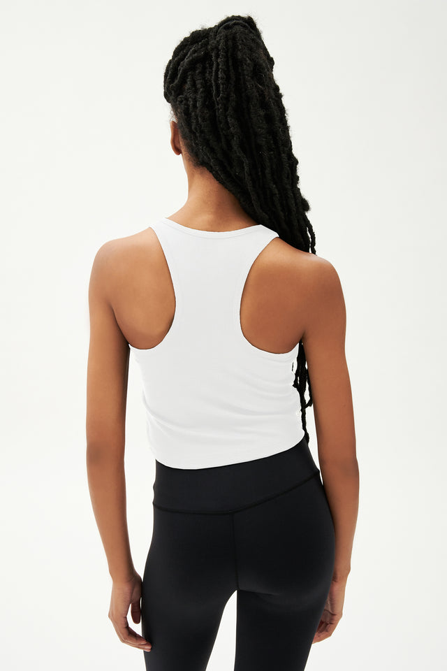 Back view of girl wearing a white cropped tank top and black leggings 
