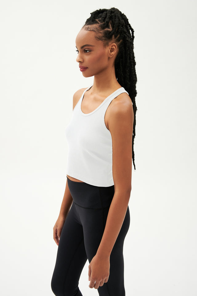 Side view of girl wearing a white cropped tank top and black leggings 