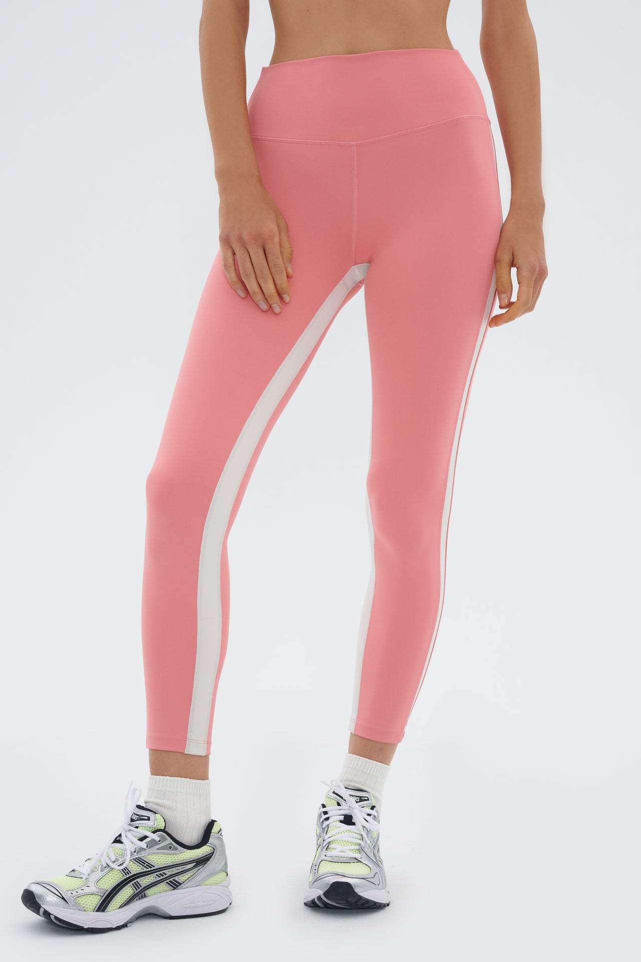 Front view of girl wearing light pink leggings with a white stripe down the side and inseam and multicolored shoes