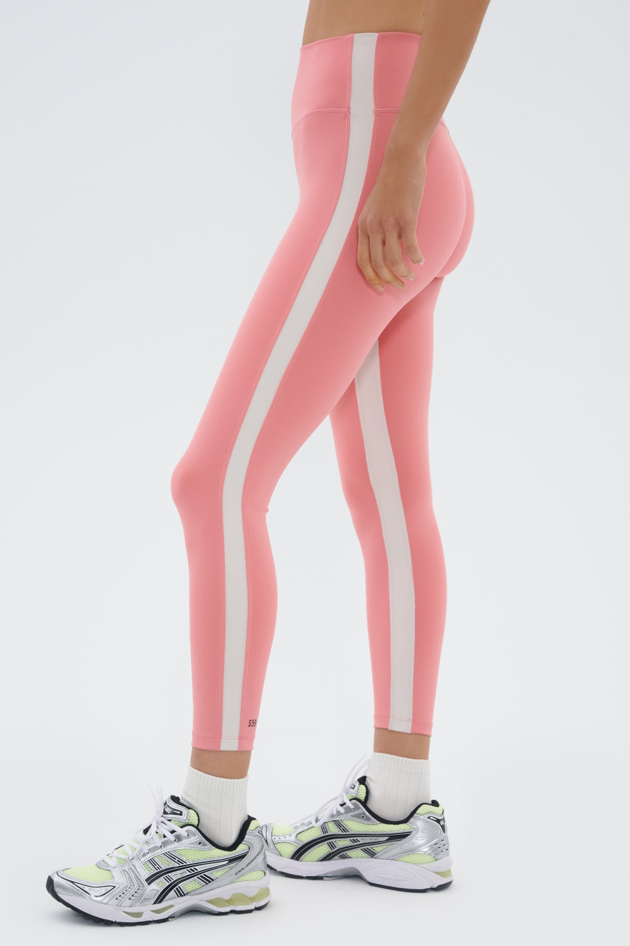Side view of girl wearing light pink leggings with a white stripe down the side and inseam and multicolored shoes