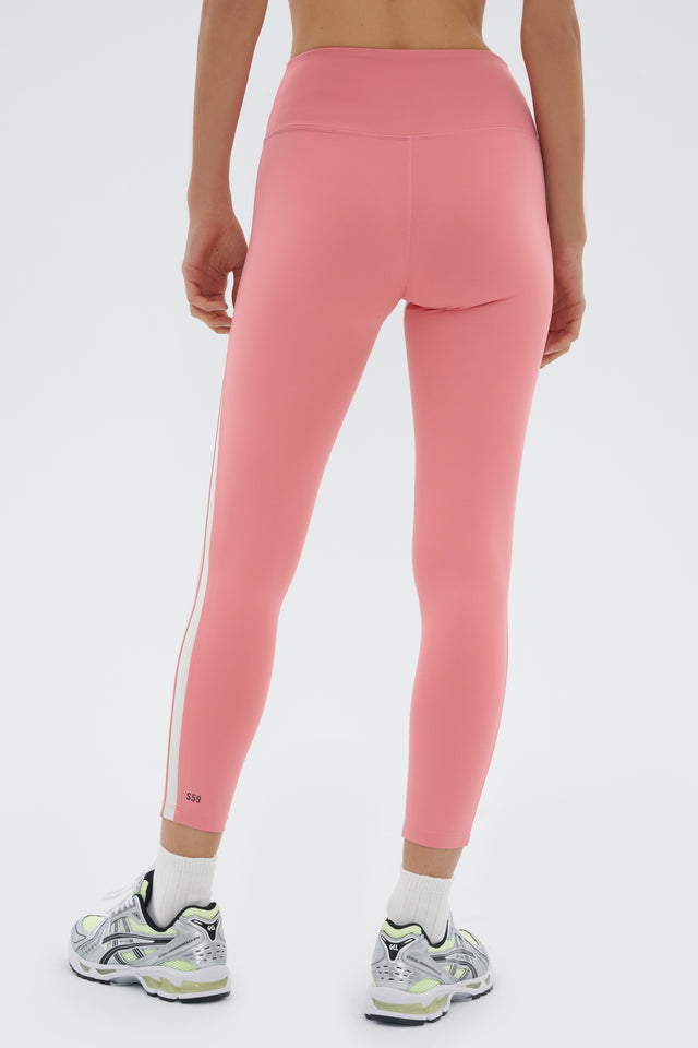 Back view of girl wearing light pink leggings with a white stripe down the side and inseam and multicolored shoes