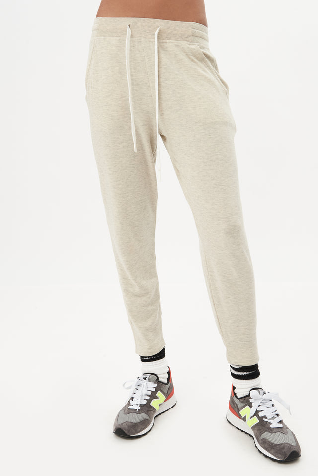 Front view of woman wearing a light gray sweatpant with tapered leg and above ankle length with white drawstring and side hip pockets. Paired with dark gray shoes with a bright green and red color block.