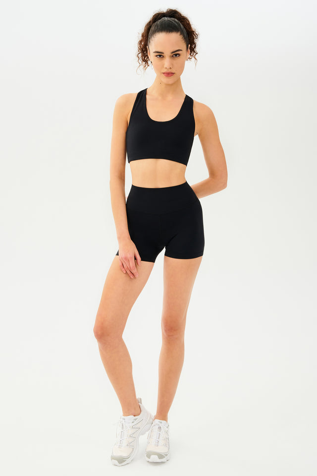 Full front view of girl wearing black shorts with black sports bra and white shoes
