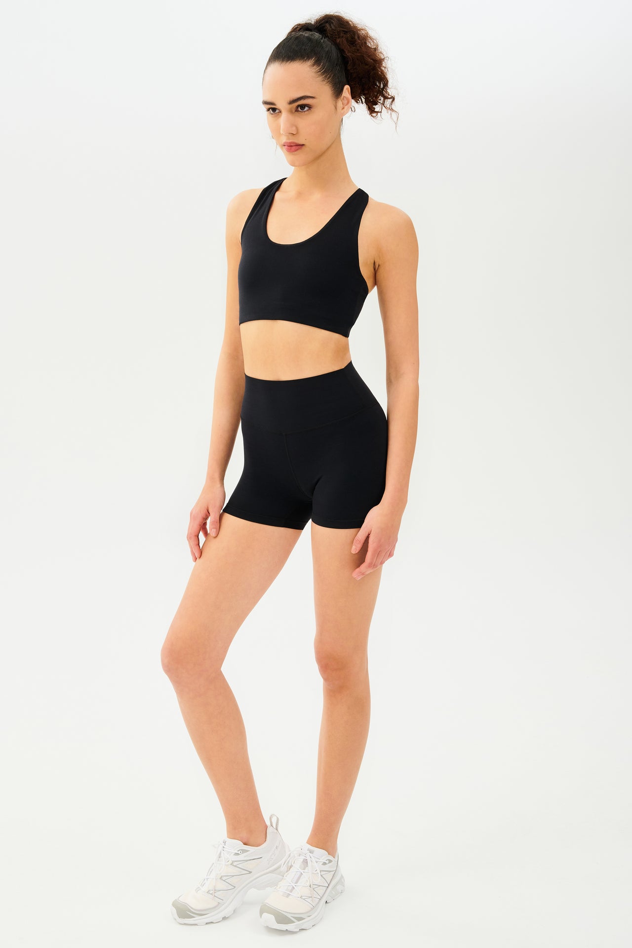 Full side view of girl wearing black shorts with black sports bra and white shoes
