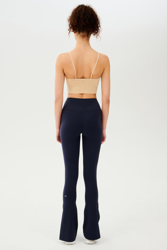 The back view of a woman wearing navy flared leggings and a Splits59 Loren Seamless Cami - Nude.