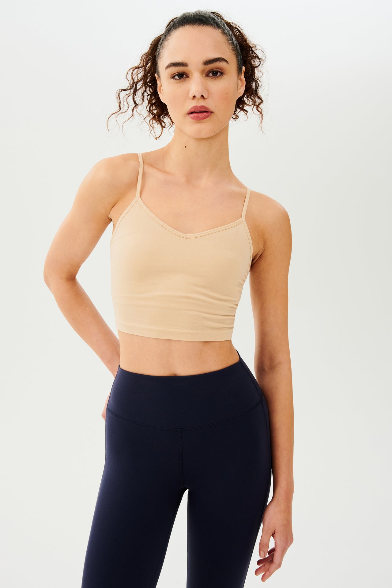 The model is wearing a Loren Seamless Cami - Nude by Splits59 with a built-in shelf bra and black leggings made from chafe-free fabric.