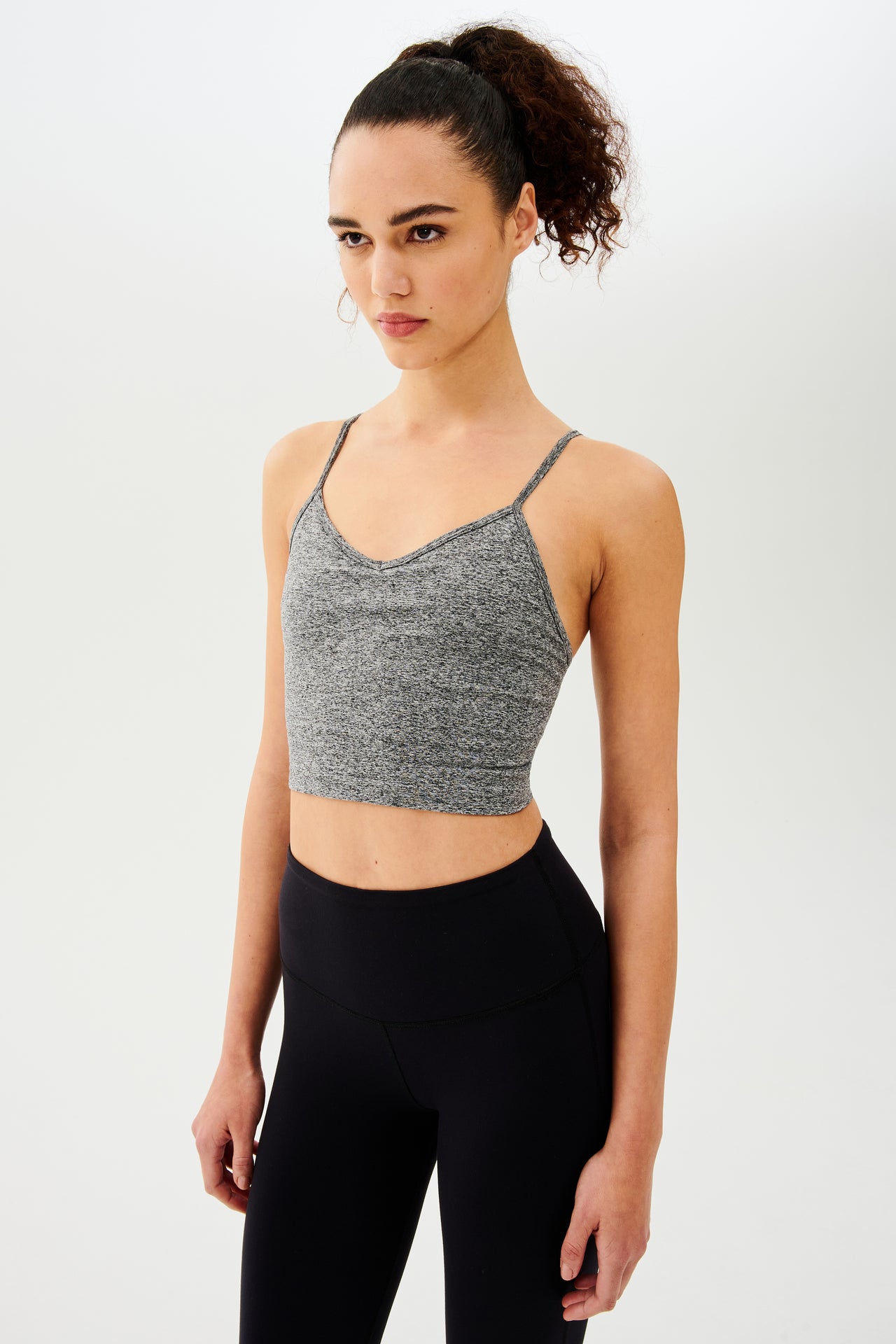 A woman wearing a Splits59 Loren Seamless Cami in Heather Grey with a built-in shelf bra and black leggings.