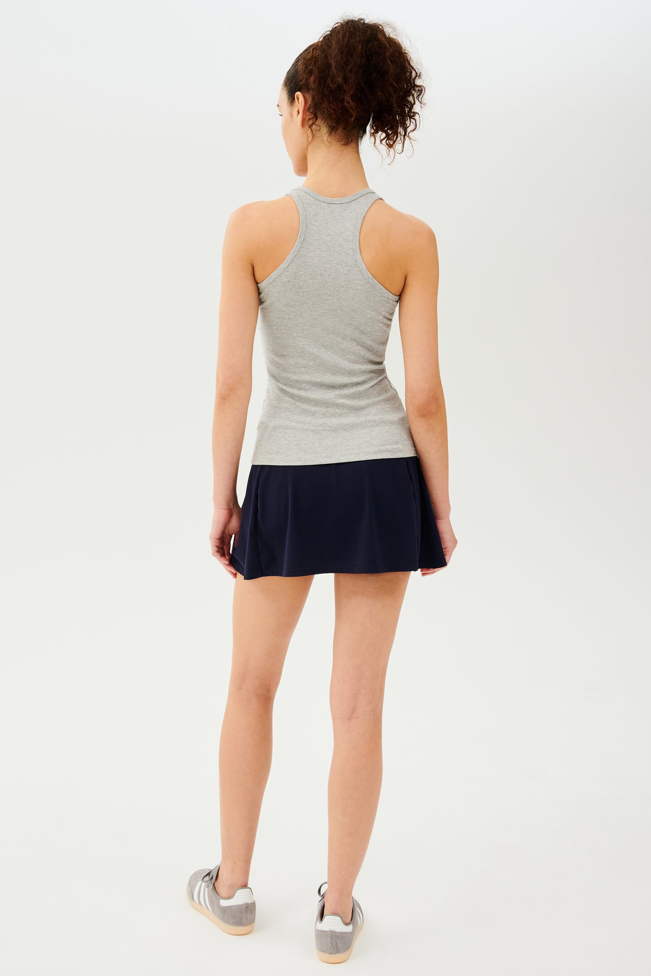 Full back view of girl wearing a light grey tank top and black skirt with grey shoes