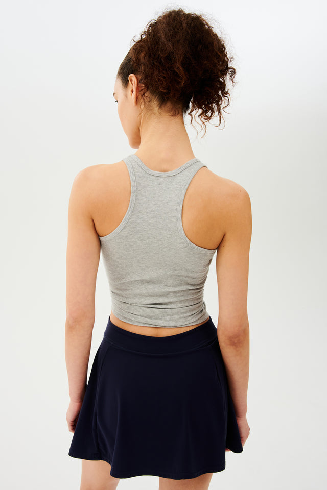 Back view of girl wearing a light grey tank top and black skirt 