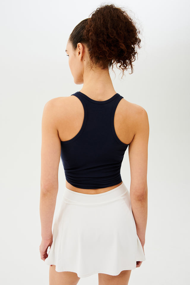 Back view of woman with dark curly hair in a ponytail wearing a white skort and a black tank top