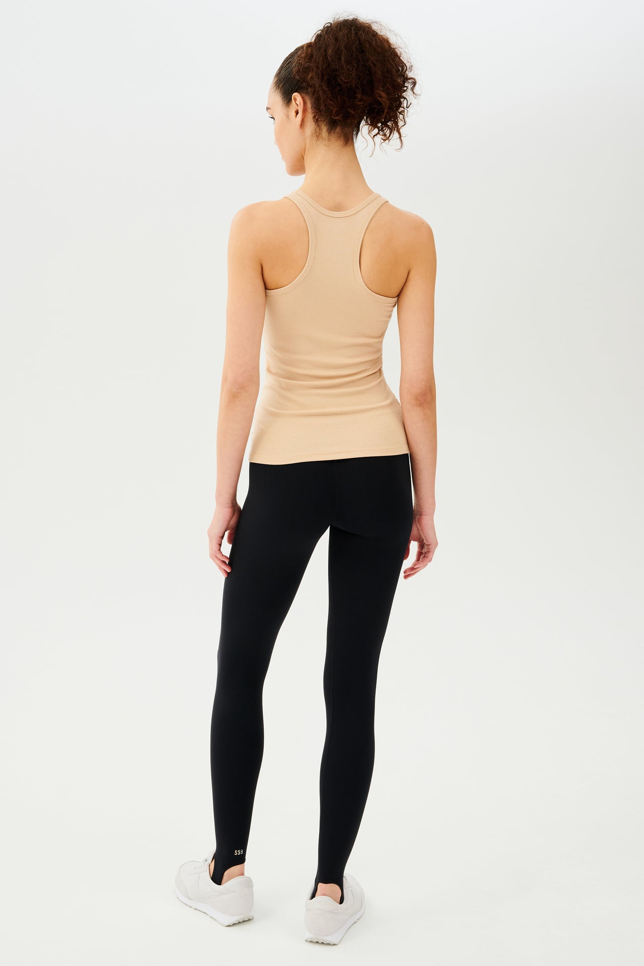 Full back view of girl wearing a yellowish brown ribbed tank top and black leggings with white shoes