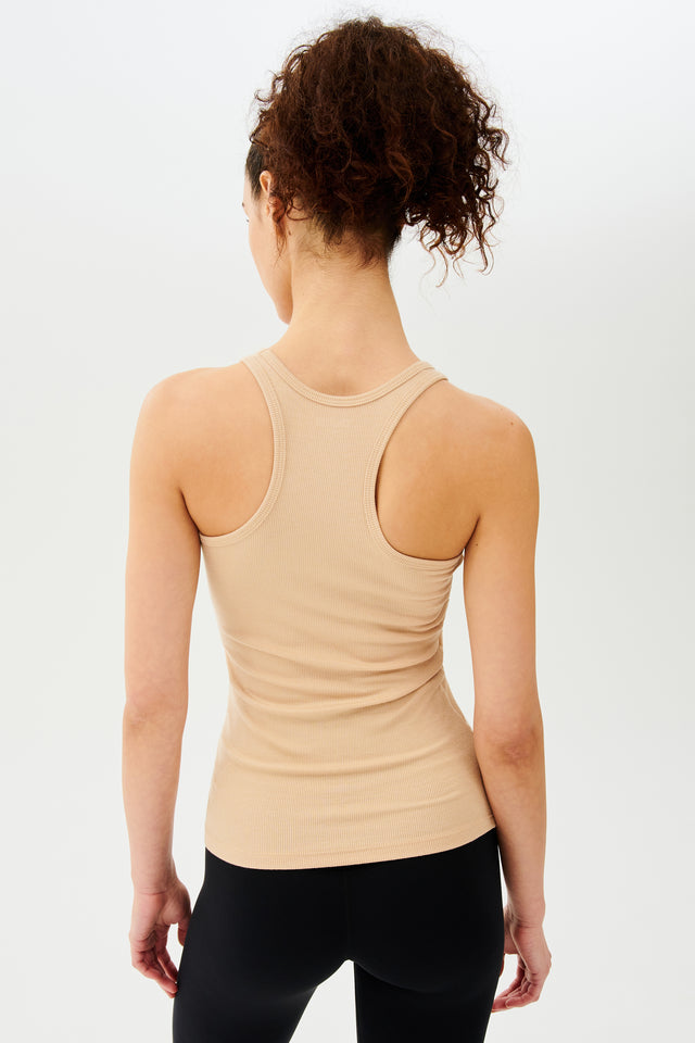 Back view of girl wearing a yellowish brown ribbed tank top and black leggings 