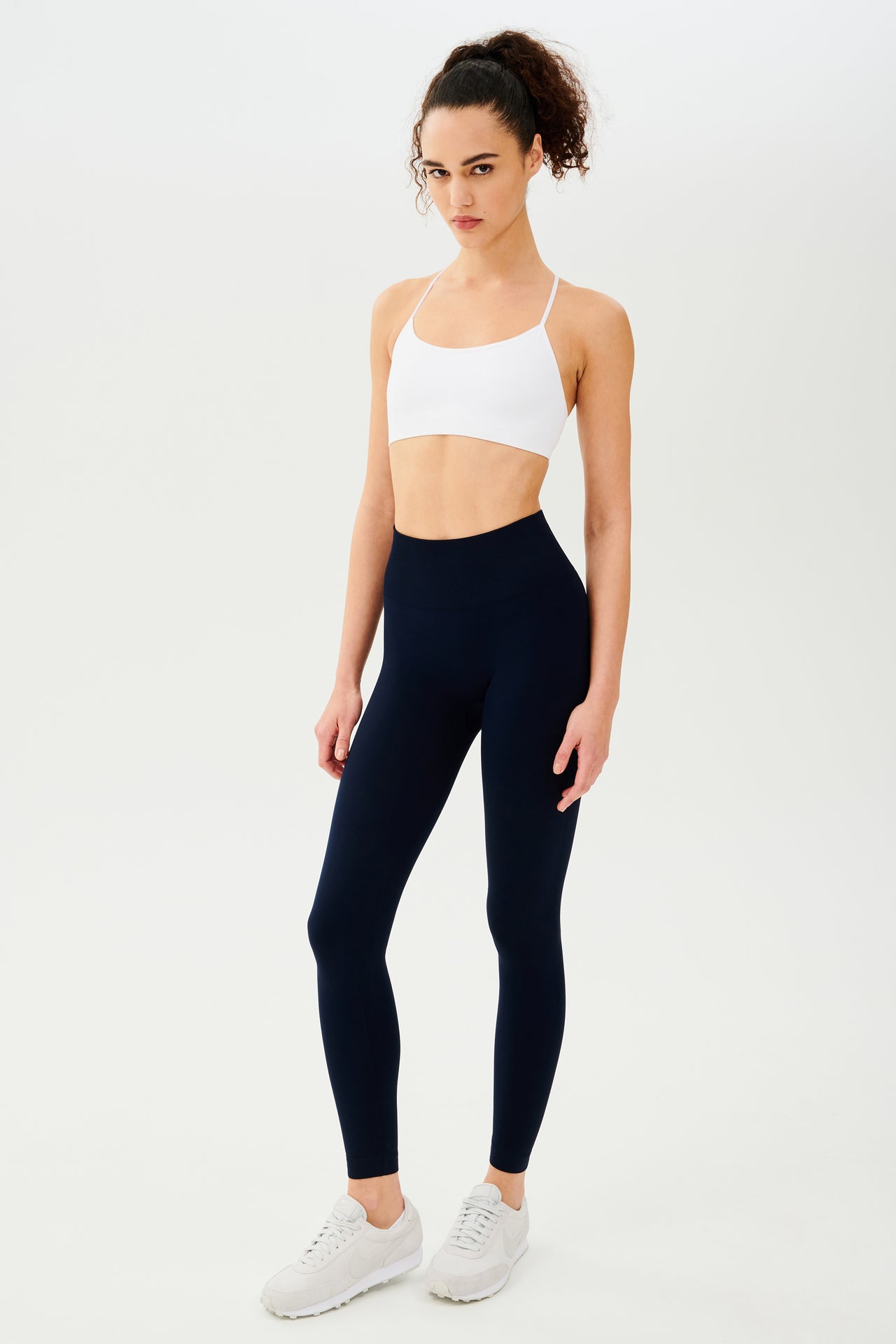 The model is wearing a white top and SPLITS59 navy Loren Seamless High Waist Full Length leggings, perfect for enhancing your workout experience.