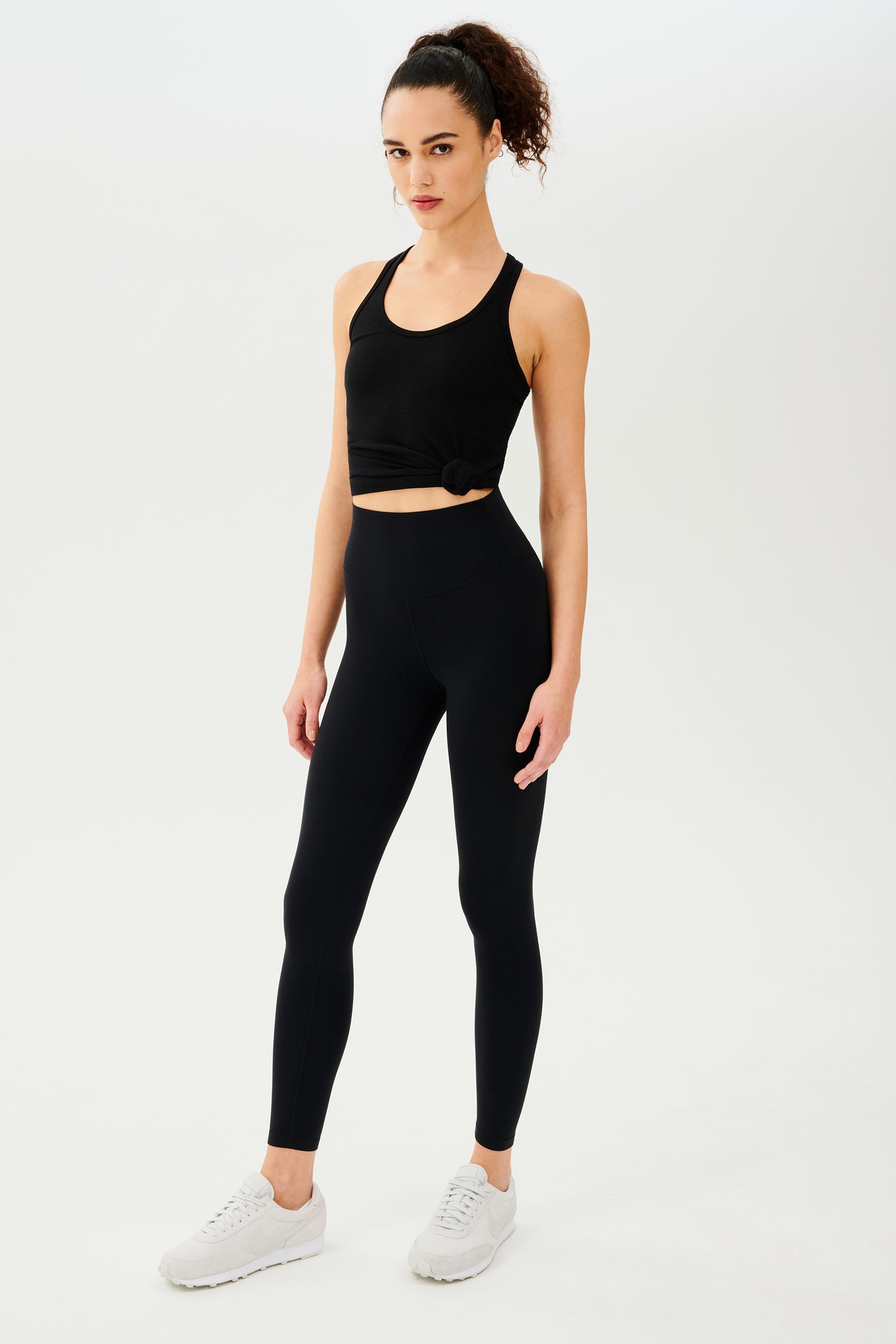 Full side view of girl wearing a black tank top and black leggings with white shoes