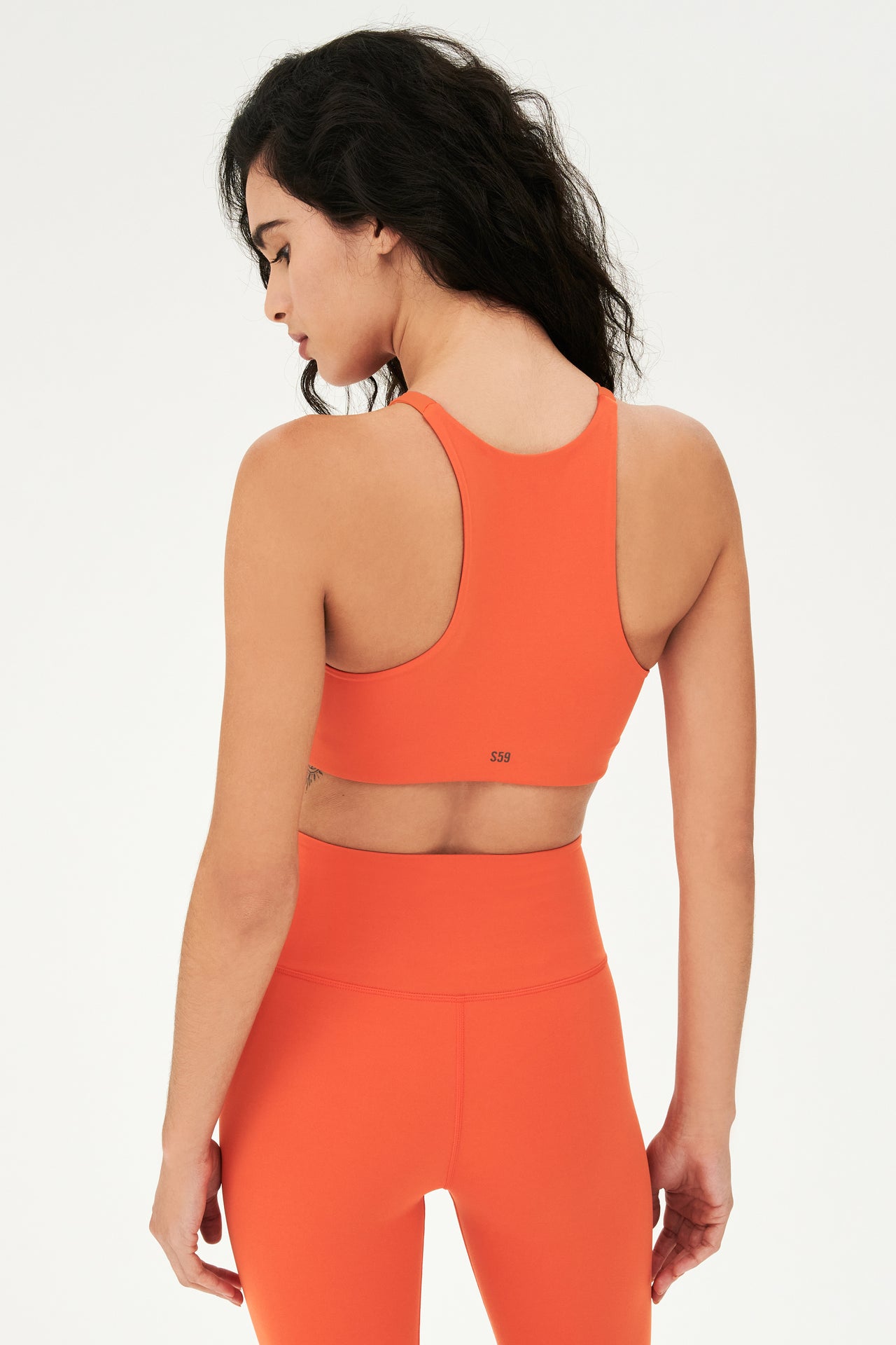 Back view of girl wearing orange sports bra that stops at collarbone and orange leggings