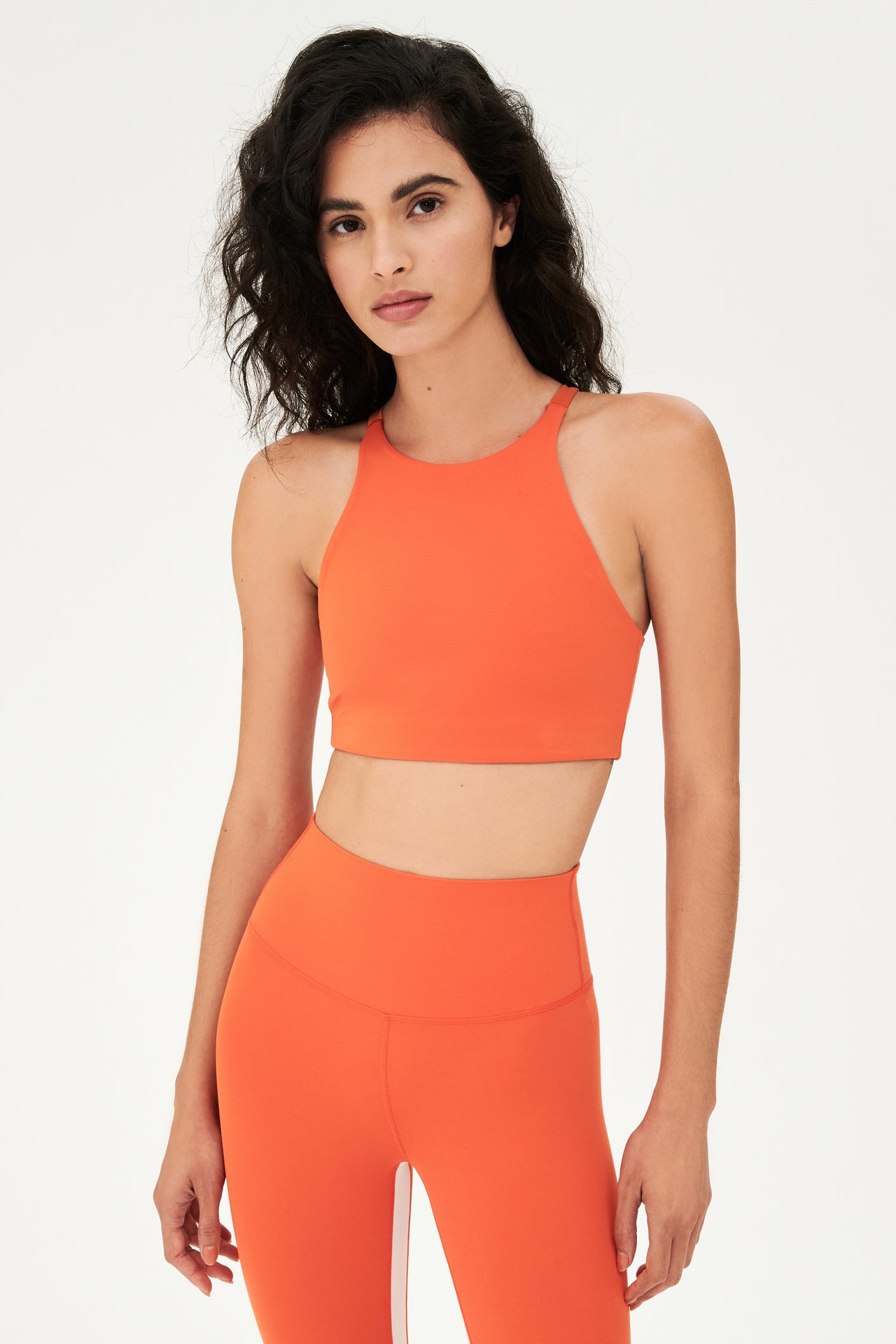 Front view of girl wearing orange sports bra that stops at collarbone and orange leggings