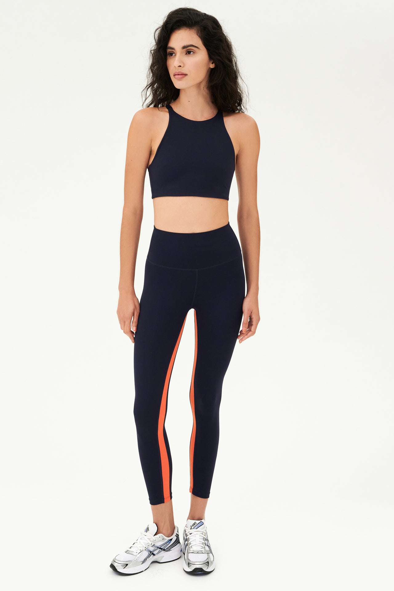 Full front view of girl wearing dark blue sports bra that stops at collarbone and dark blue leggings with white shoes
