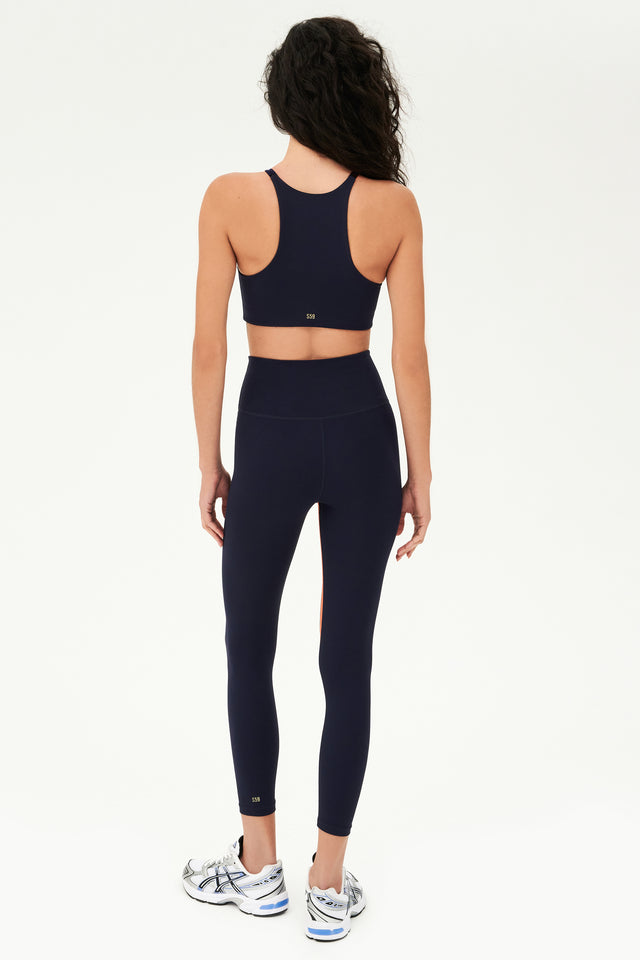 Full back view of girl wearing dark blue sports bra that stops at collarbone and dark blue leggings with white shoes