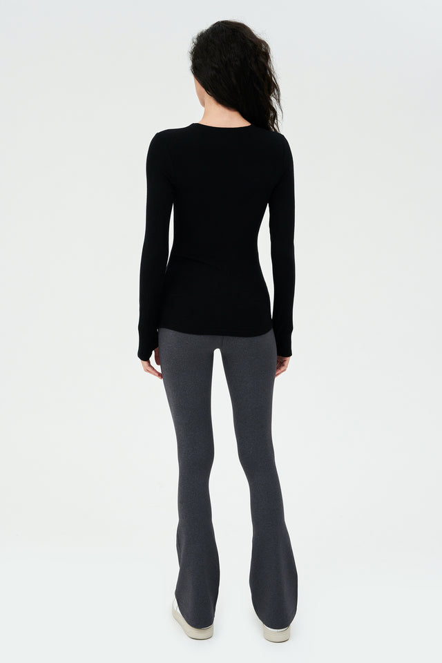 The back view of a woman wearing a SPLITS59 Louise Rib Long Sleeve - Black, ideal for gym workouts, and grey leggings.