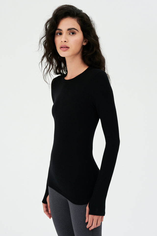 A woman wearing a SPLITS59 Louise Rib Long Sleeve - Black shirt and leggings is ready for her gym workouts.