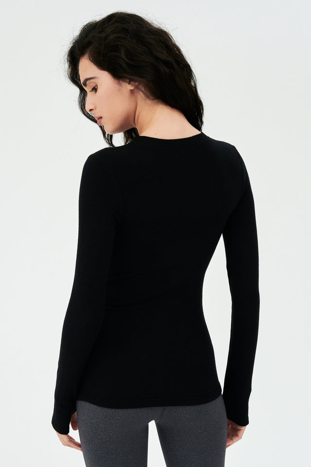 The back view of a woman wearing a SPLITS59 Louise Rib Long Sleeve - Black, ideal for layering during gym workouts.